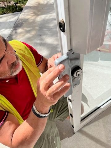 A man in a red shirt and yellow safety vest fixing the lock on a glass door.