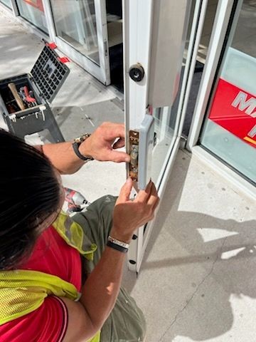 Person repairing a glass door lock with tools on the ground, wearing a safety vest.