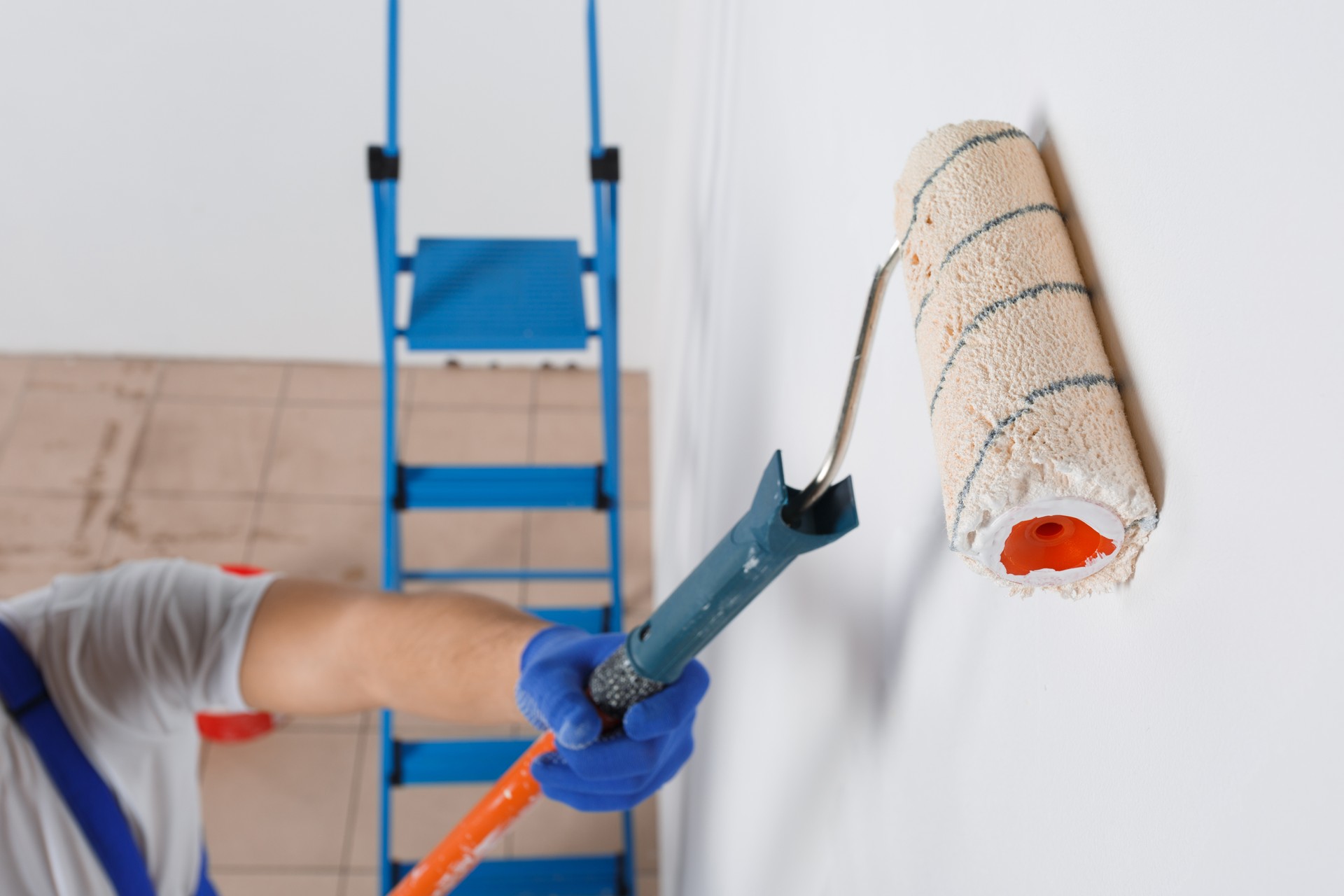 A man in gloves paints a wall with a roller for paint. Close-up. View from above.