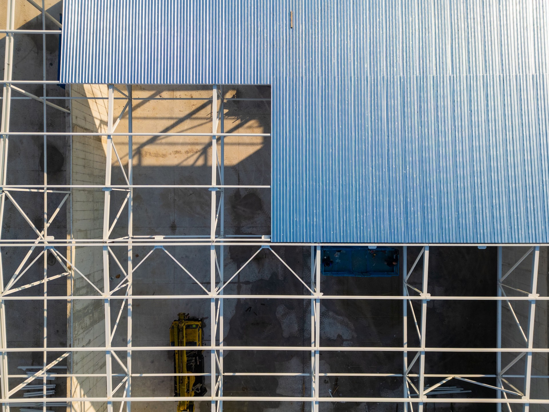 A construction site with a partially built warehouse featuring a steel framework and metal roof. Workers and heavy machinery operate on-site, showcasing industrial progress and structural development